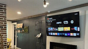 Un salon moderne avec un téléviseur à écran plat fixé au mur, une porte noire et un plancher en bois.