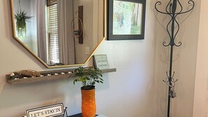 Un comptoir d’accueil avec une pancarte indiquant « RESTONS À L’INTÉRIEUR », un miroir, un tableau encadré, une plante en pot et un porte-manteau.