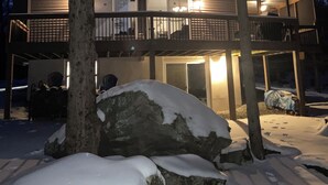 Uma casa de dois andares com varanda, rodeada por terreno e árvores cobertas de neve.