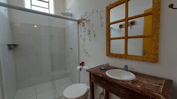 A bathroom with a glass shower enclosure, a wooden vanity with a sink, and a mirror with a decorative frame.