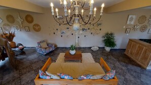 A spacious living room with a large wooden sofa, a small side table, a chandelier, and various wall decorations. - Rancho da Serra Pousada (Tiradentes)