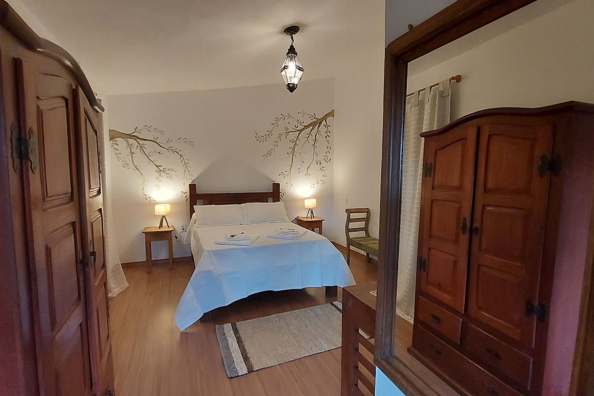 Un dormitorio con cama, dos mesitas de noche con lámparas, un armario de madera y un panel decorativo con motivos de hojas.
