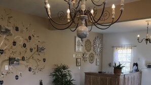 A cozy living room with a wooden sofa, a coffee table, and a chandelier. There are wall decorations and a window with curtains. - Rancho da Serra Pousada (Tiradentes)