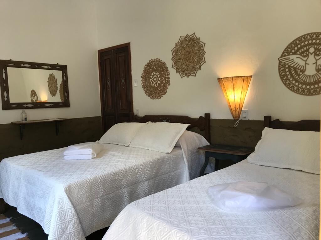 A hotel room with two beds, a mirror, decorative wall art, and a wall-mounted lamp.
