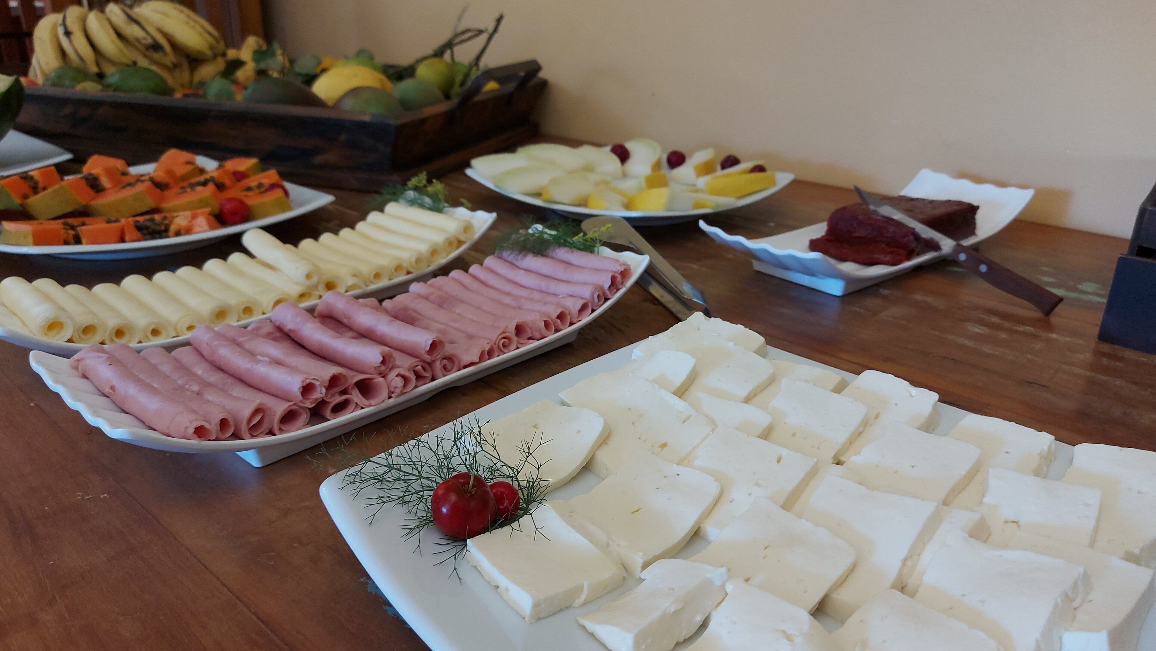 Diversos alimentos como frutas en rodajas, quesos y embutidos dispuestos sobre una mesa de madera.