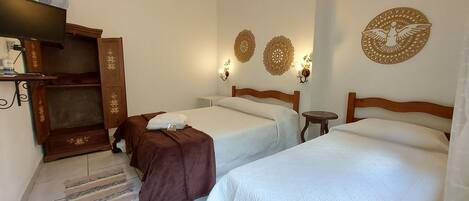 A hotel room with two beds, a wooden wardrobe, a small table, and decorative wall sconces.