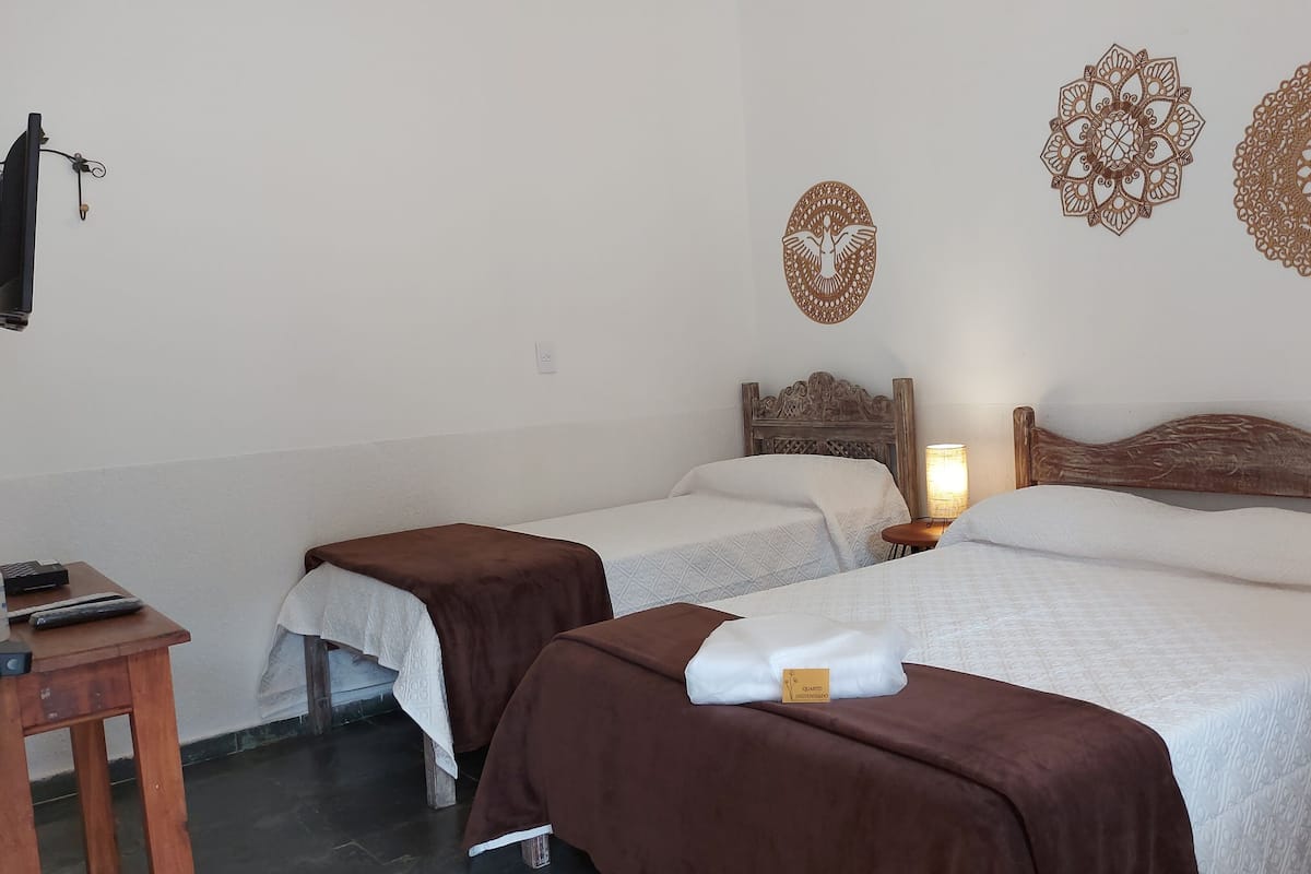 Habitación de hotel con dos camas, cabecero de madera, mesita de noche con lámpara y decoración en la pared.