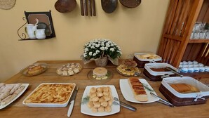 A buffet table with various baked goods, including pastries, bread, and a cake, arranged on a wooden table. - Rancho da Serra Pousada (Tiradentes)