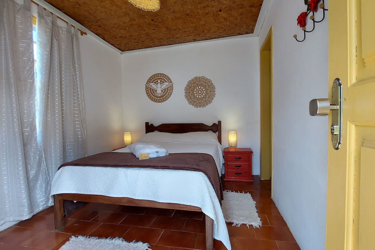 Una cama bien hecha con cabecera de madera, dos lámparas de noche y una mesita de noche roja.