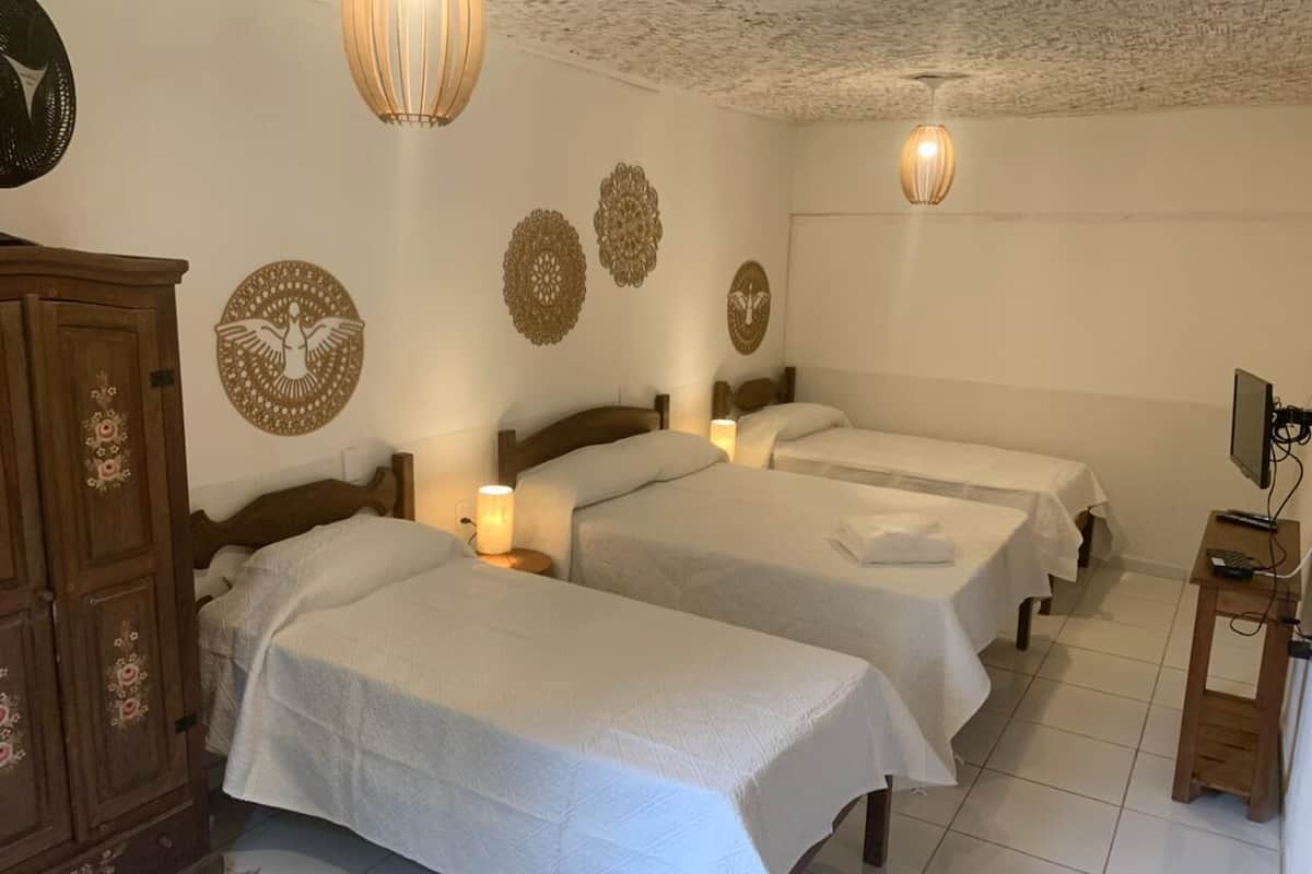 Habitación de hotel con tres camas, un armario de madera, detalles decorativos en la pared y un televisor sobre un mueble de madera.