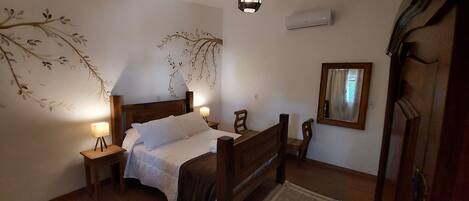 Un dormitorio con una cama de madera, mesitas de noche con lámparas, aire acondicionado de pared y un espejo.