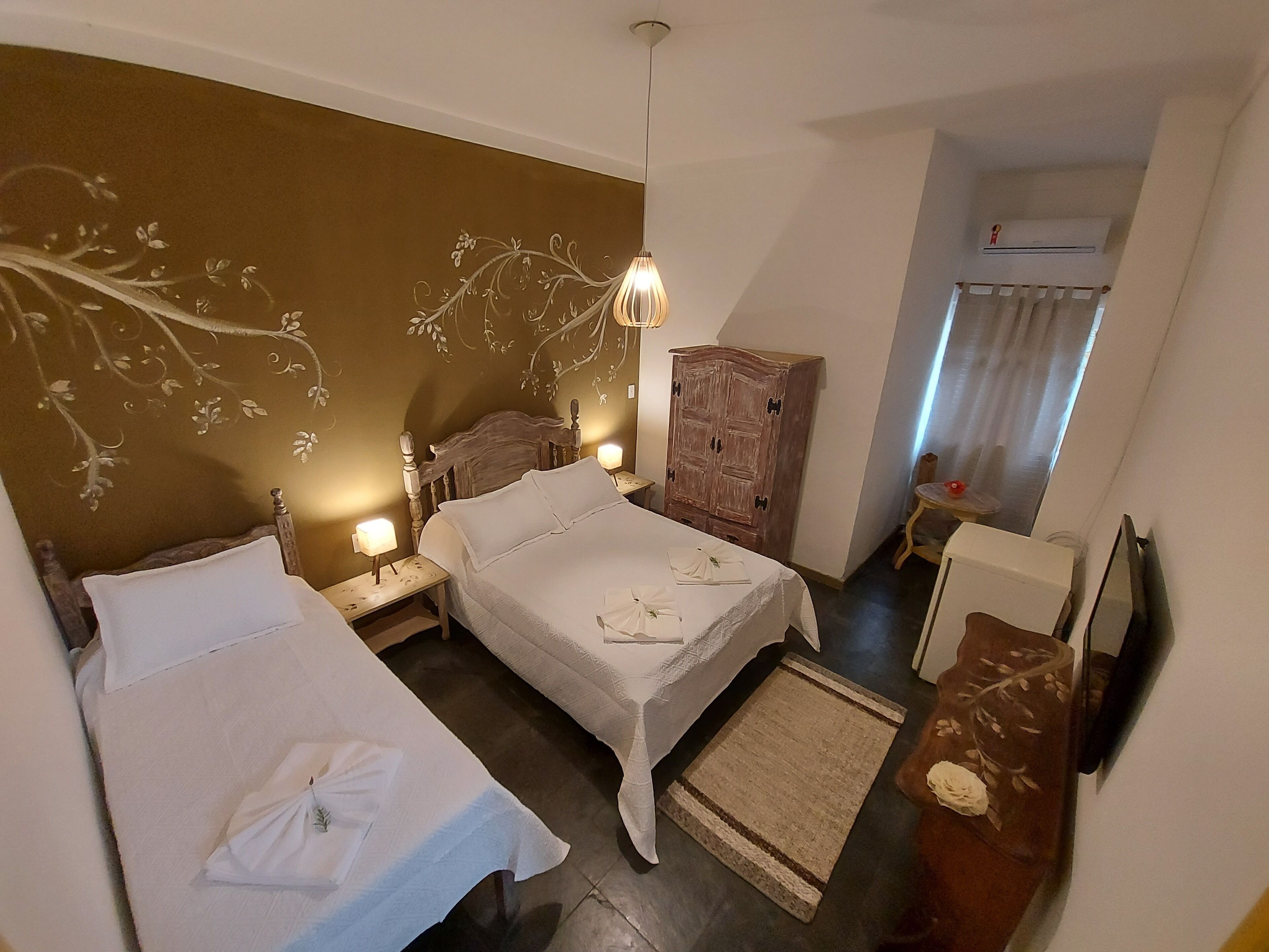 A hotel room with two beds, a wooden wardrobe, a desk, and a television.