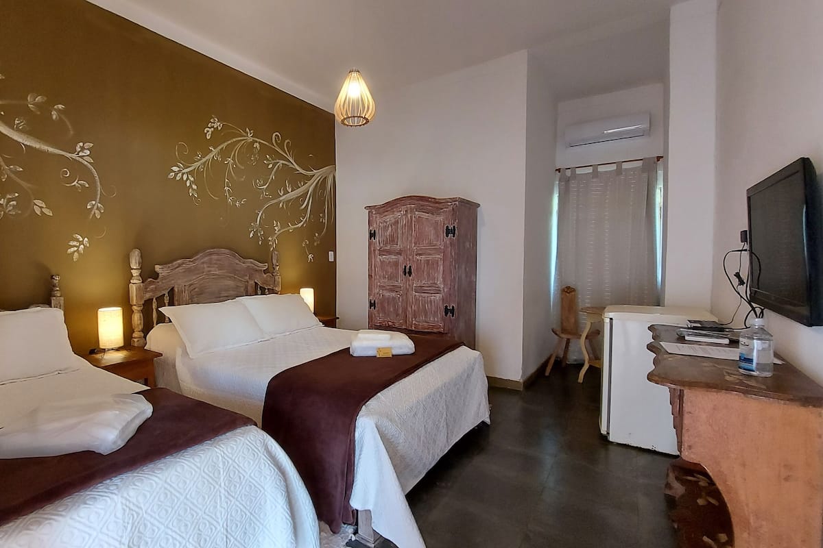 Habitación de hotel con dos camas, un armario de madera, un escritorio con televisor y una decoración de pared.