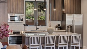A modern kitchen with a central island, stainless steel appliances, and a view of the outdoors.