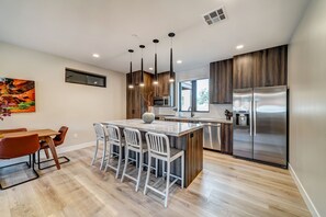 A modern kitchen with a central island, stainless steel appliances, and a dining area with a wooden table and chairs.
