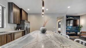 A modern kitchen with a marble island, wooden cabinets, and a stainless steel refrigerator.