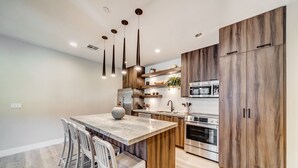 A modern kitchen with a marble island, wooden cabinets, stainless steel appliances, and pendant lighting.