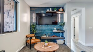 A modern living room with a stone wall, a mounted TV, a wooden table, and a seating area with chairs.
