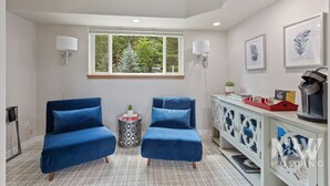 A modern room with two blue armchairs, a white cabinet with decorative glass doors, a window with a view of trees, and wall-mounted lamps. - Luxurious Echo Bay Retreat—Hot Tub, Fire Pit, Ping Pong, Chess, Bikes & Stunning Views Await! (Harrison)