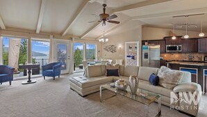 A spacious living room with a large sectional sofa, a glass coffee table, and a ceiling fan. There is a view of a kitchen and a balcony with a scenic view. - Luxurious Echo Bay Retreat—Hot Tub, Fire Pit, Ping Pong, Chess, Bikes & Stunning Views Await! (Harrison)