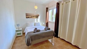 Une chambre à coucher avec un lit, des tables de chevet, une lampe, une fenêtre avec des rideaux et un tableau au mur.