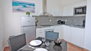Une cuisine moderne avec des armoires blanches, un réfrigérateur en acier inoxydable, un four à micro-ondes et une cuisinière à gaz. On y trouve une table à manger avec des chaises et une petite plante en pot posée sur le réfrigérateur.