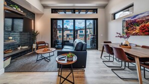 A modern living room with a fireplace, a dining area, and a large sliding glass door leading to a balcony with a mountain view. - LaFave-Luxury Villa at Zion: Orderville Canyon (Springdale)