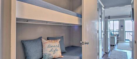 A bunk bed with a pillow labeled "Beach Life" and a door leading to a hallway.