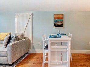 Un salon avec un canapé gris, une table blanche avec des sets de table bleus et un tableau accroché au mur.