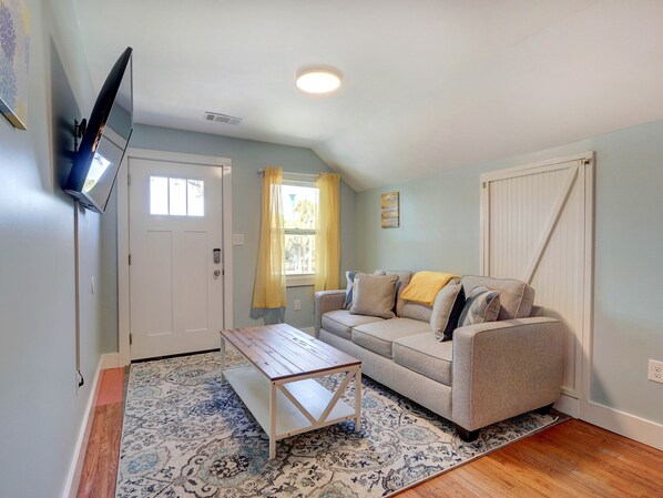 Un salon comprenant un canapé, une table basse, un téléviseur fixé au mur, une fenêtre avec des rideaux et un tapis à motifs.