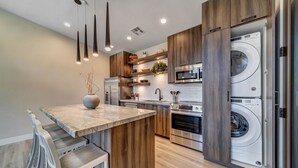 Een moderne keuken met een marmeren aanrechtblad, roestvrijstalen apparatuur, houten keukenkastjes en een ingebouwde wasmachine en droger.