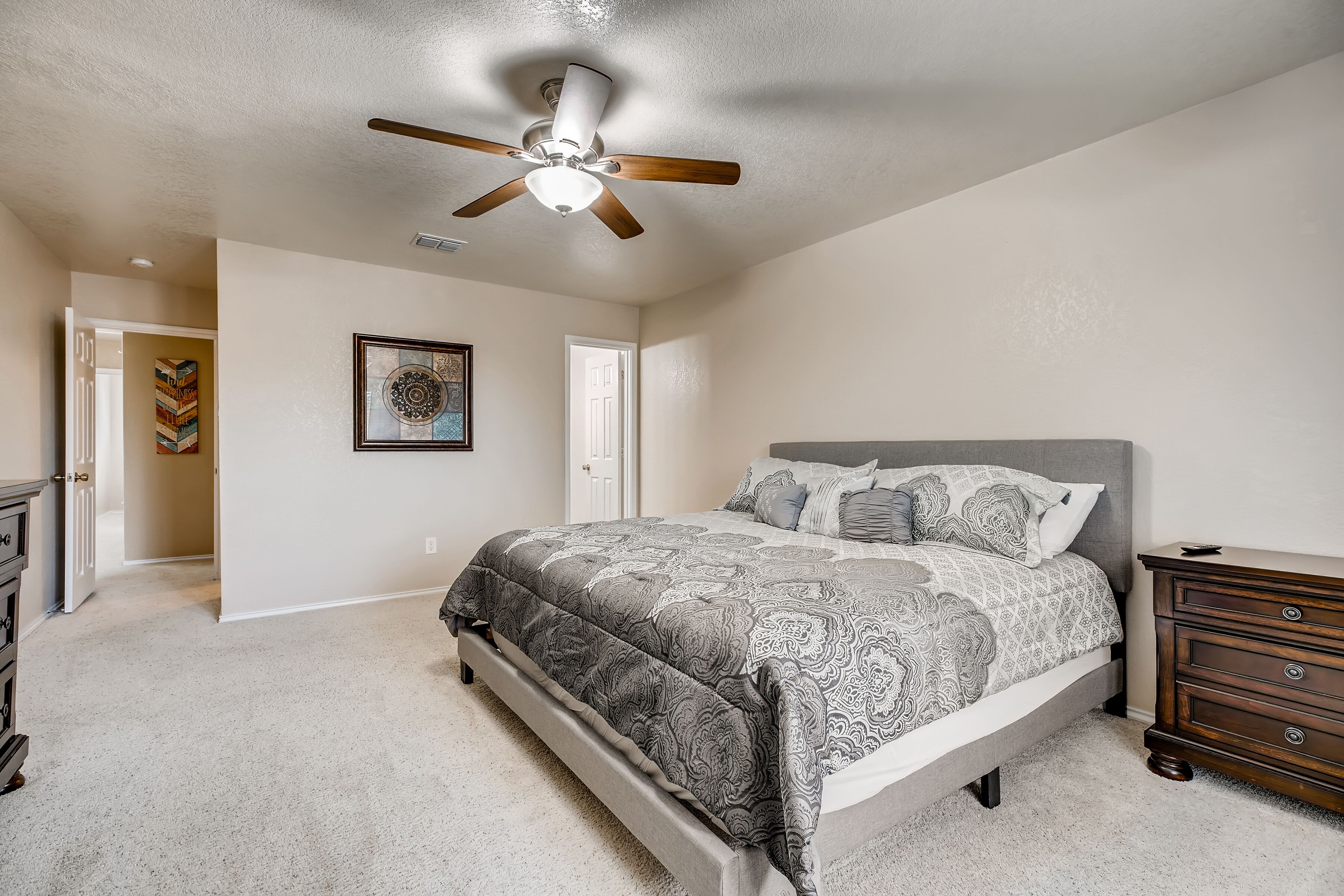 A bedroom with a bed, a dresser, a ceiling fan, and a door.