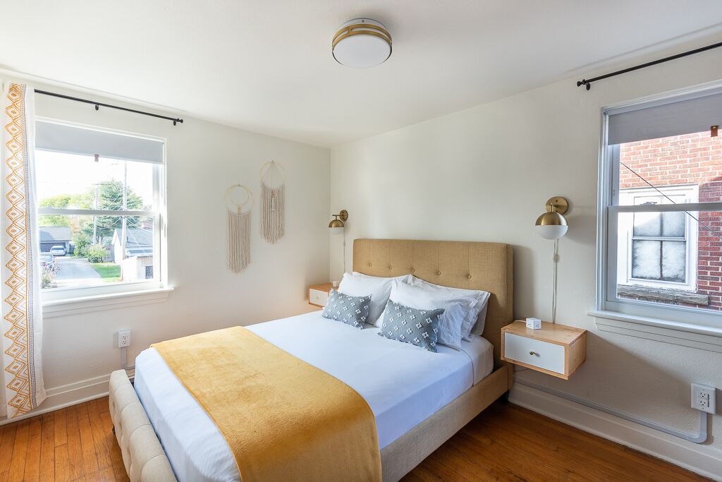 Een slaapkamer met een bed, nachtkastjes, een hanglamp en een raam met gordijn.
