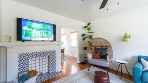 Een woonkamer met een televisie waarop 'Welcome to ERIE' staat, een open haard met decoratieve tegels, een rieten stoel, een blauwe bank en een plafondventilator.