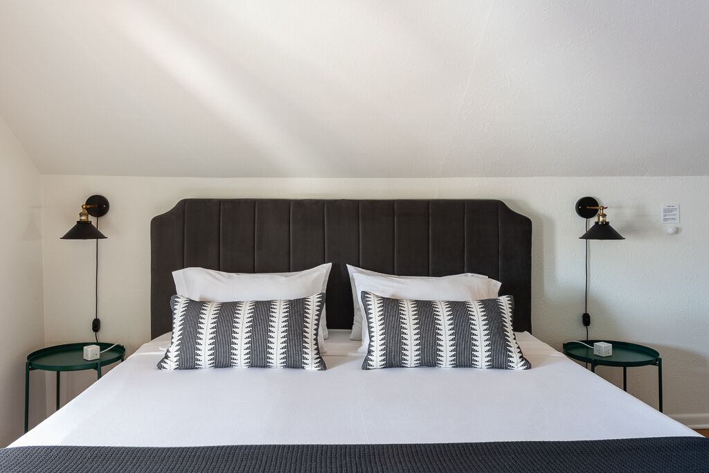 A neatly made bed with a dark headboard, two bedside tables with lamps, and patterned pillows.