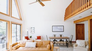 A spacious living room with a large sofa, a dining table, and a ceiling fan.