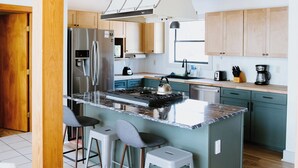 A modern kitchen with a central island, stainless steel appliances, and light-colored cabinetry.