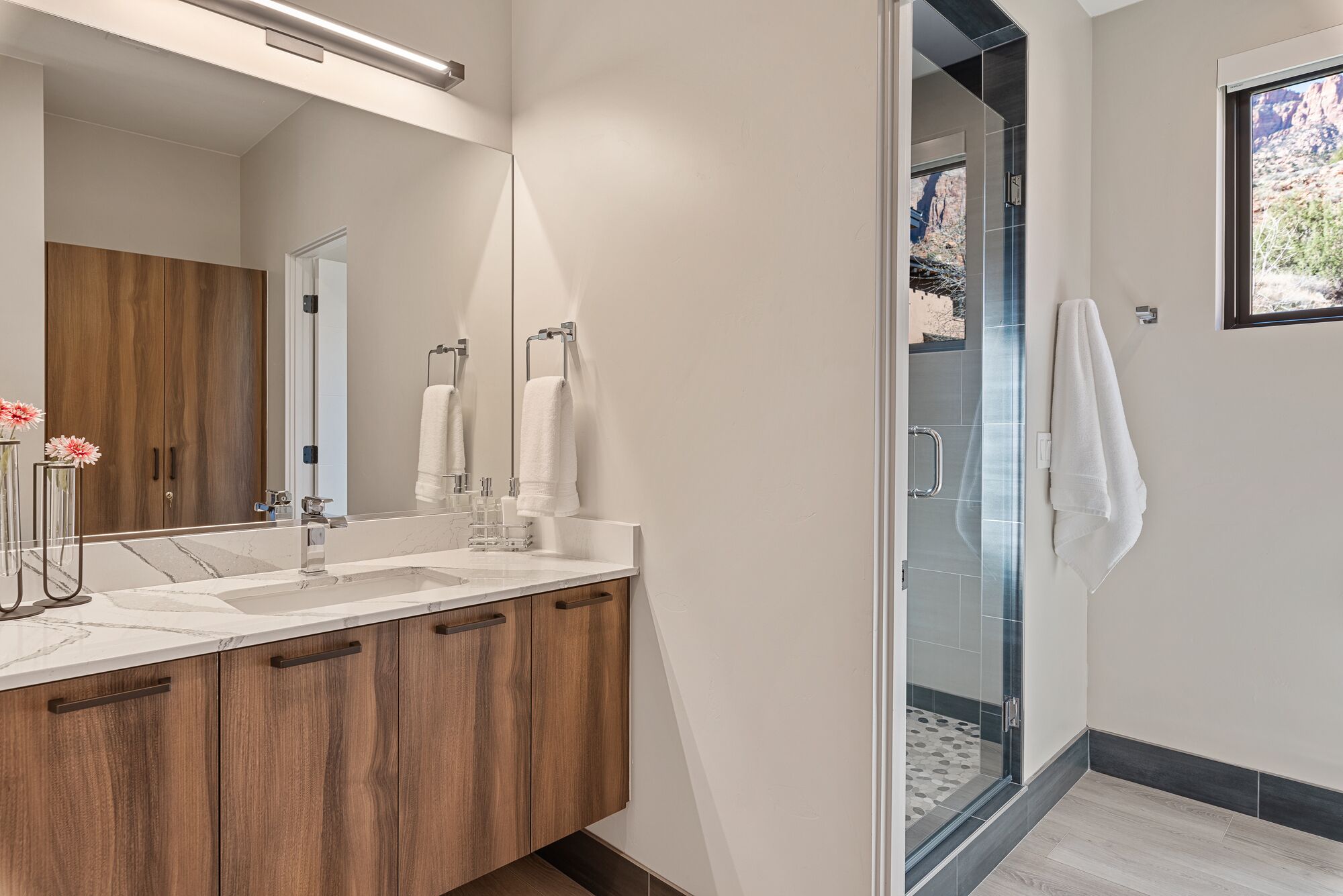 Un baño moderno con tocador de madera, un espejo grande y una cabina de ducha de vidrio.