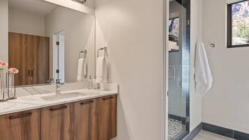 Un baño moderno con tocador de madera, un espejo grande y una cabina de ducha de vidrio.