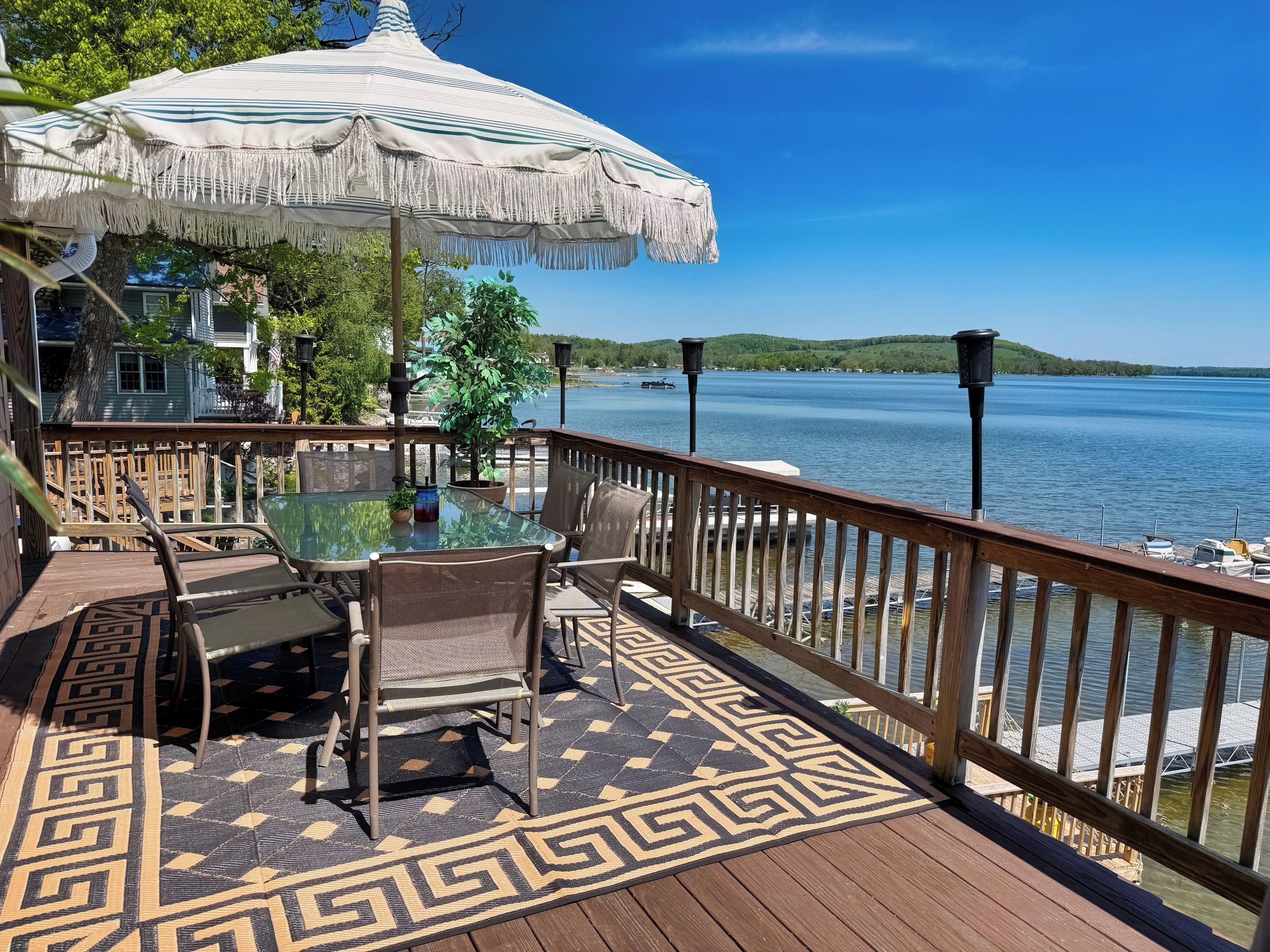 A deck with a glass table, chairs, and a patterned rug.