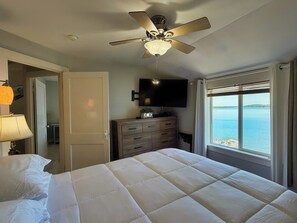 Een slaapkamer met een bed, een plafondventilator, een televisie, een dressoir en een raam met uitzicht op het water.