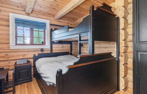 A bunk bed with a desk and chair, a window with a view of trees, and wooden walls.