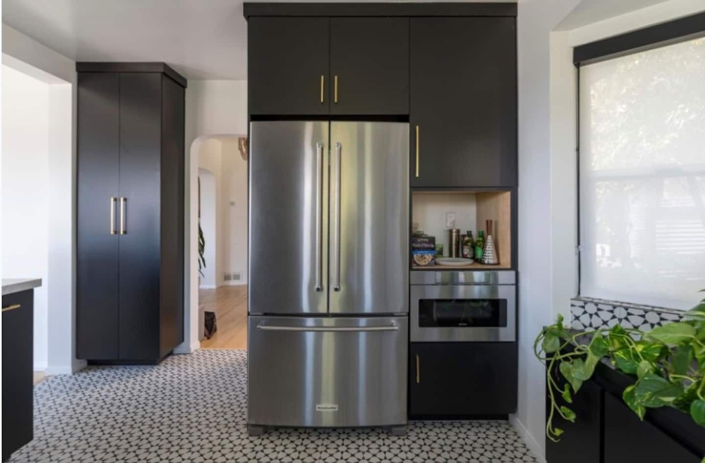 A modern kitchen with a stainless steel refrigerator, dark cabinetry, and a tiled floor.