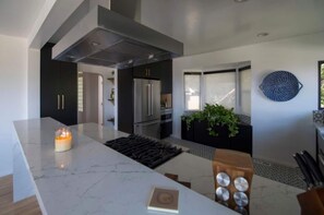 A modern kitchen with a large island, stainless steel appliances, and a black backsplash. - Come stay at a Very Special Place (Los Angeles)