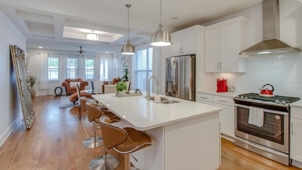 A modern kitchen with white cabinetry, a central island with bar stools, stainless steel appliances, and pendant lighting.