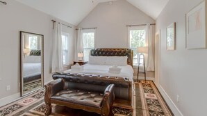 A bedroom with a large bed, a chest of drawers, a vanity, and a ceiling fan.