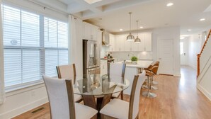 A modern kitchen with white cabinets, stainless steel appliances, and a glass dining table with chairs.