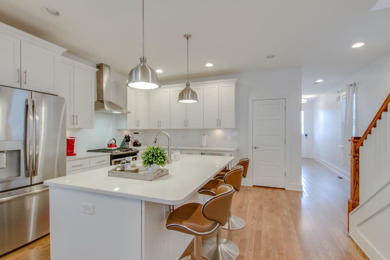 Een moderne keuken met witte kasten, roestvrijstalen apparatuur en een centraal eiland met barkrukken.