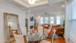 A spacious living room with a glass-top dining table, plush seating, a fireplace, and large windows.