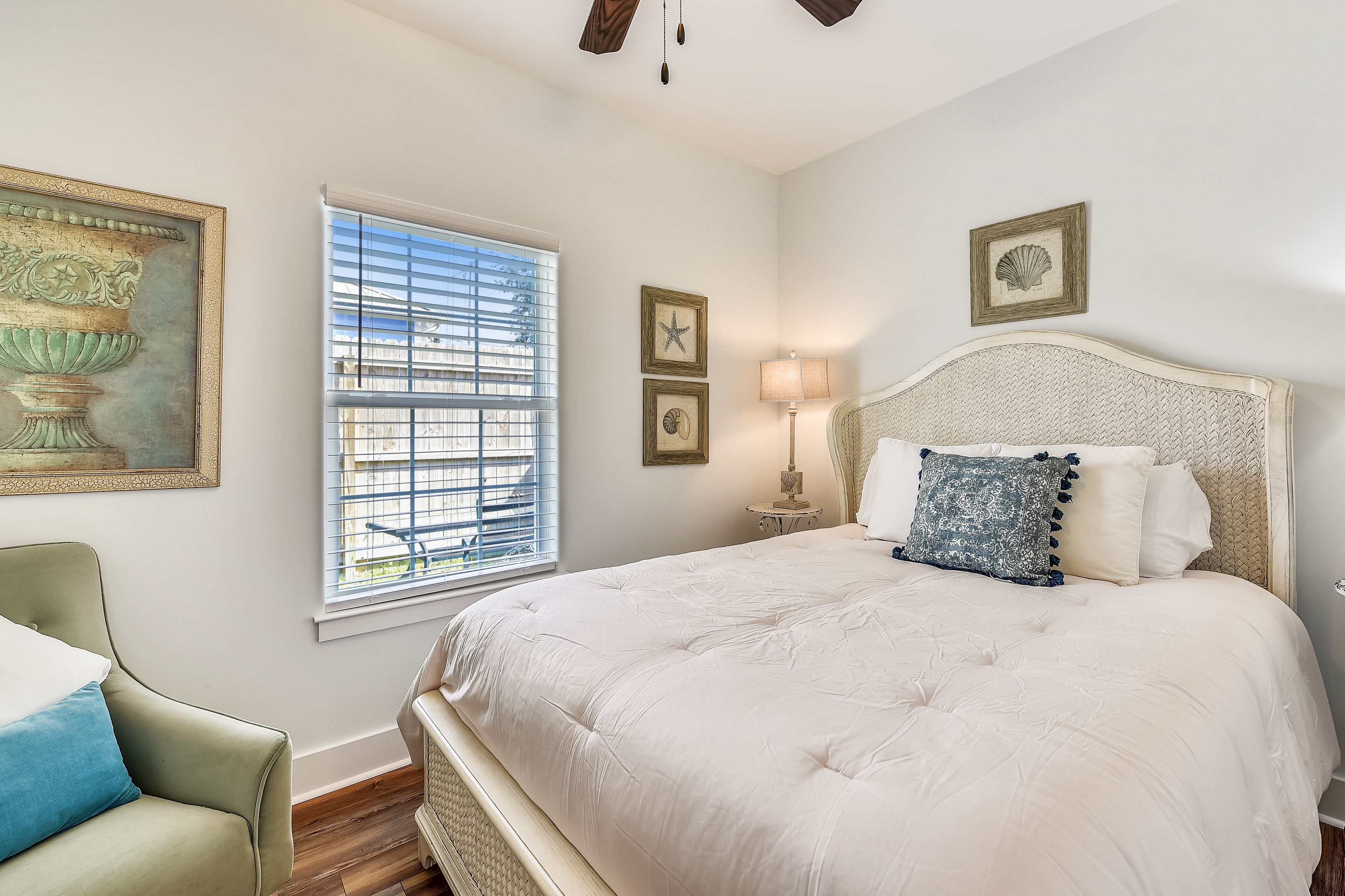 A bedroom with a large bed, a chair, a window with blinds, and wall-mounted artwork.